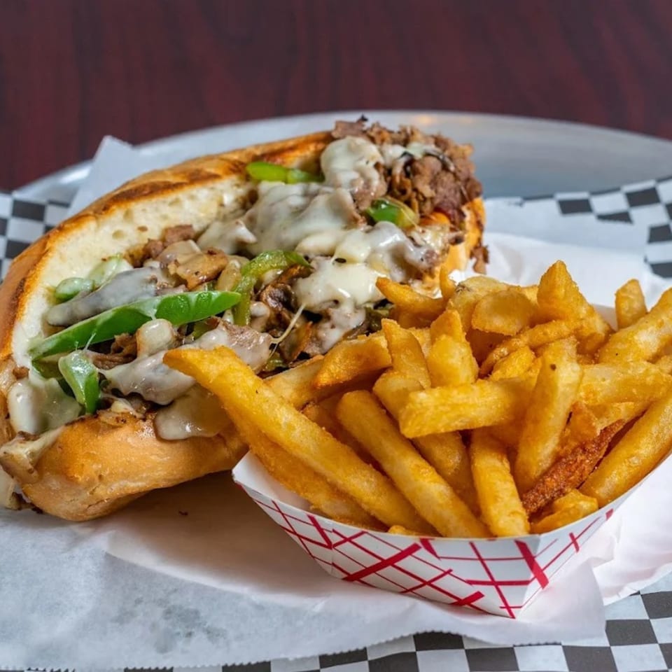 Cheesesteak sandwich with melted cheese, green peppers, and mushrooms, served with golden french fries.