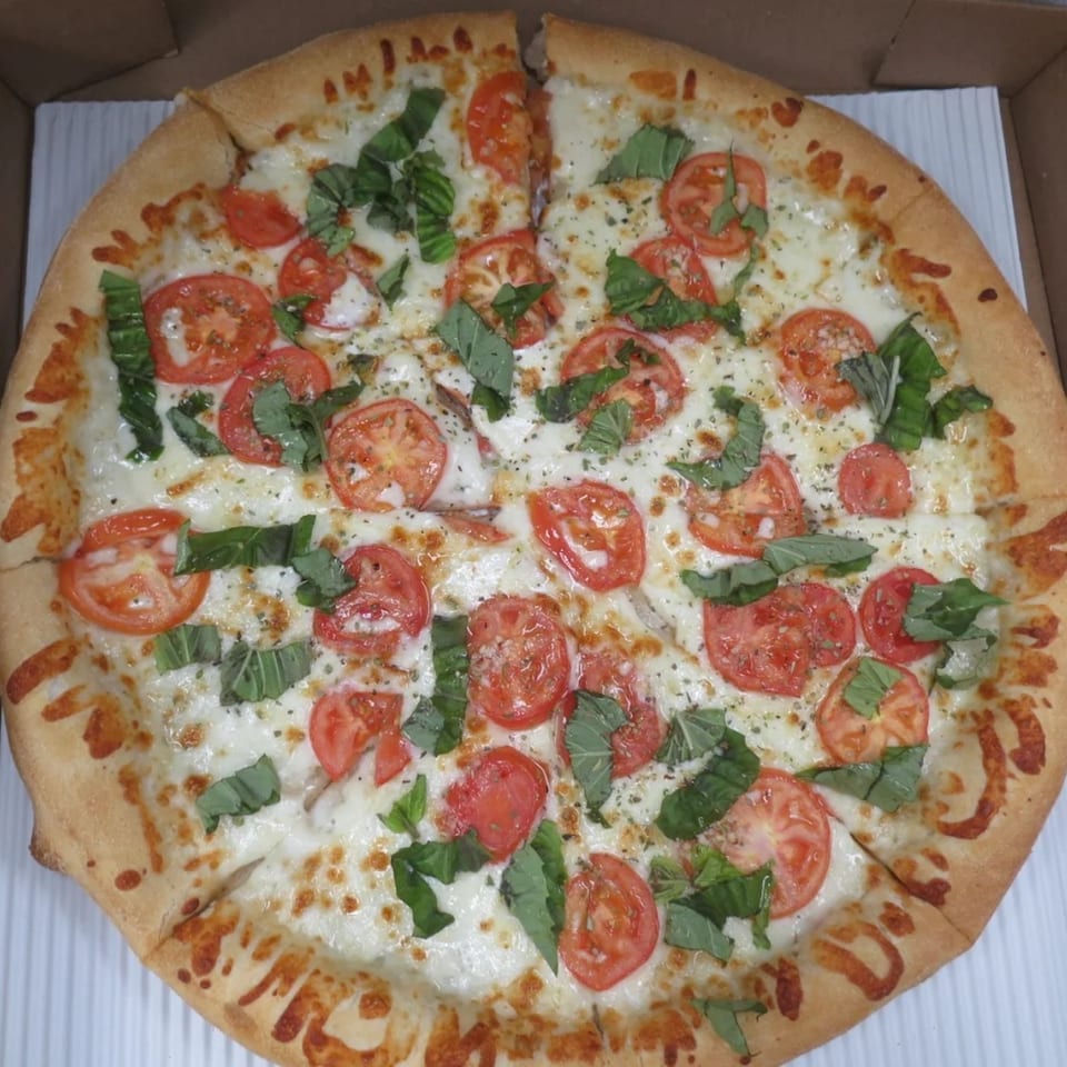 Mega Pizza's Margherita pizza, topped with fresh tomatoes, mozzarella, and basil, in a delivery box.